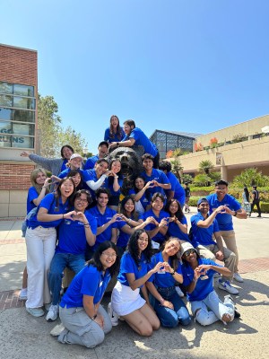Students a part of the Bruin Ambassador Program posing together at the Bruin Bear wearing their blue UCLA polo shirts and making hearts with their hands.