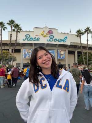 Kathryn smiling wearing a white UCLA sweatshirt standing outside the Rose Bowl while attending a UCLA football game.