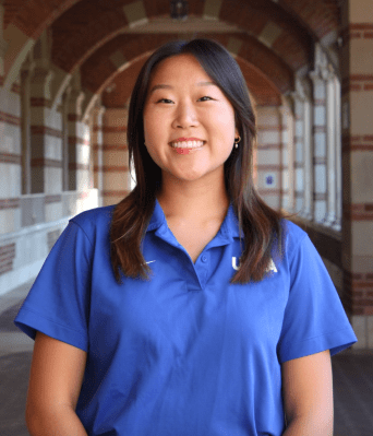 Photo of Michelle smiling confidently at Royce Hall and wearing a blue UCLA polo shirt.