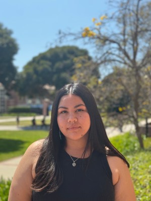 Photo of Amiee wearing a black shirt and looking the camera while outside on UCLA's campus on a sunny day. 