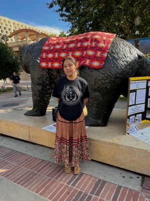 Photo of Cadence in front of the Bruin Bear statue that is draped in a printed blanket on UCLA's campus. 