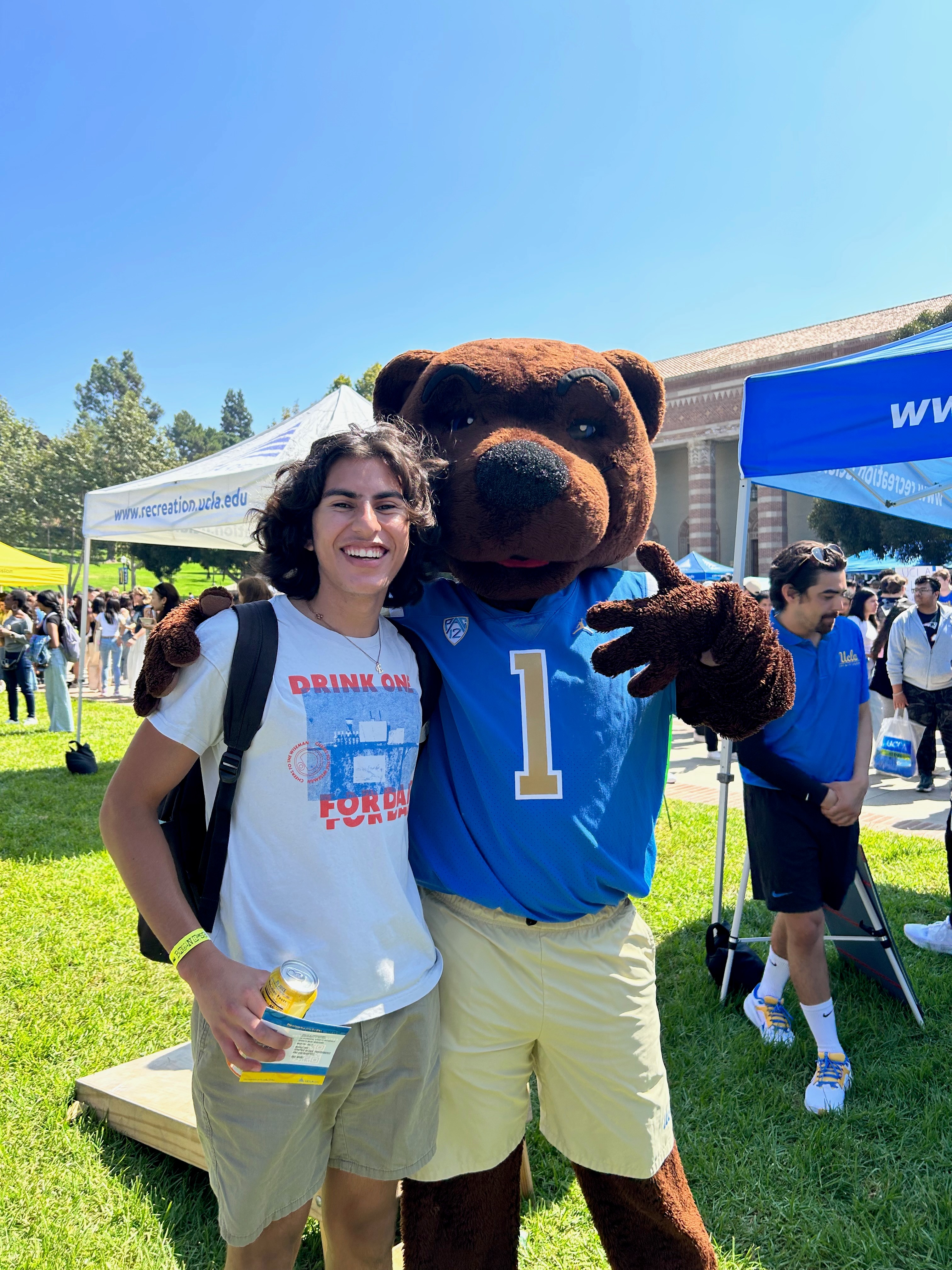 Photo of Danny at an outdoor UCLA event standing next to the Joe Bruin mascot and smiling at the camera.